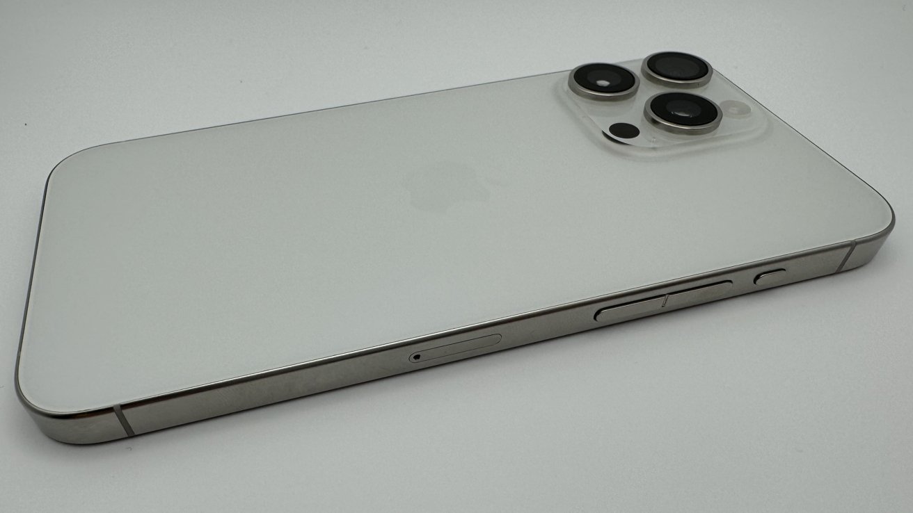 Silver smartphone with three rear cameras and volume buttons on the side, laying on a flat white surface.