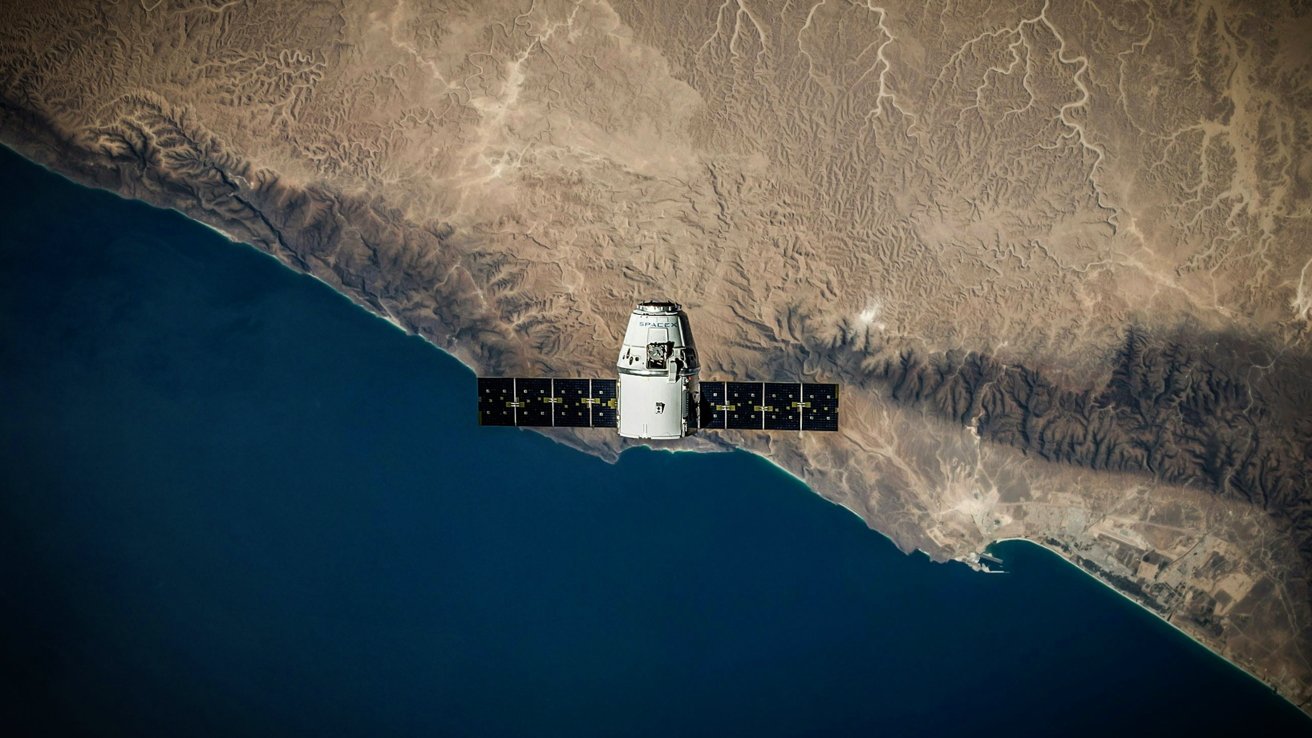 Satellite orbiting above a blue ocean and rugged, sandy coastline, showing intricate natural terrain patterns.
