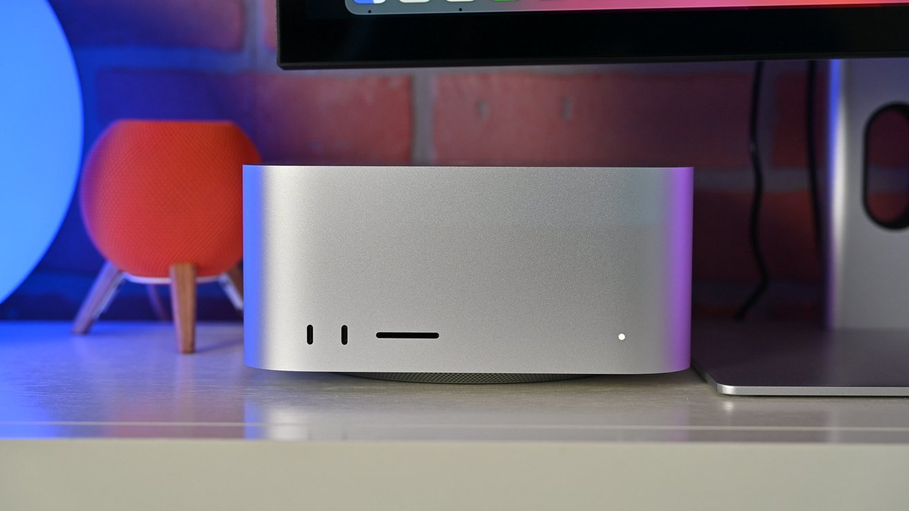 Mac Studio with ports on the front, set on a desk next to a red spherical speaker and a computer monitor.