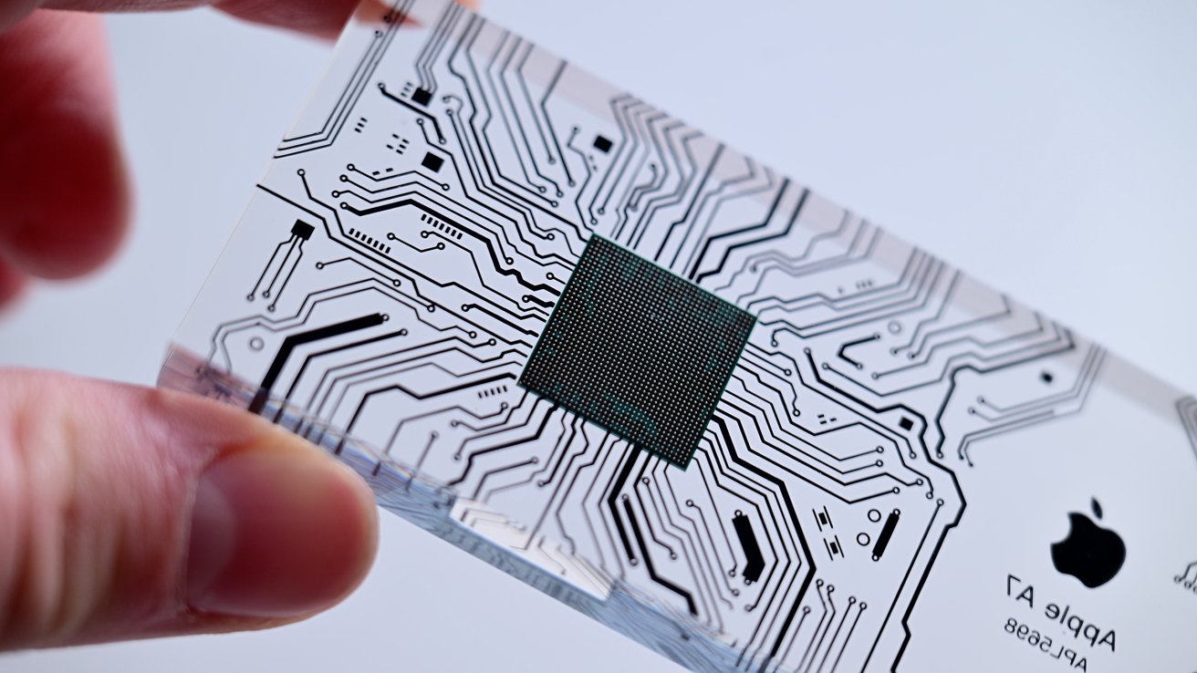 Transparent plastic card with intricate black circuit patterns and a central green square, held between two fingers.