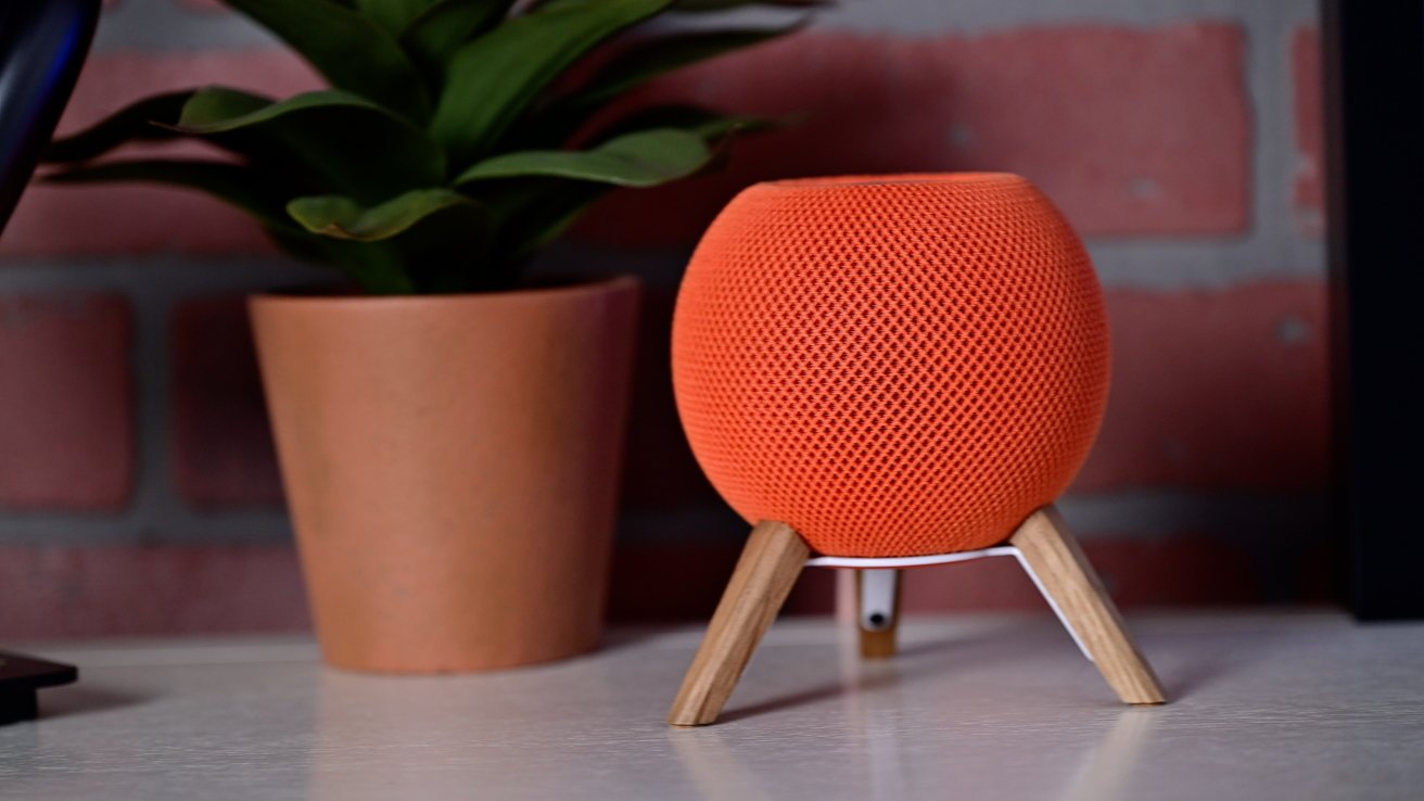 A black spherical smart speaker mounted on a wall near a window, with a wooden surface below.