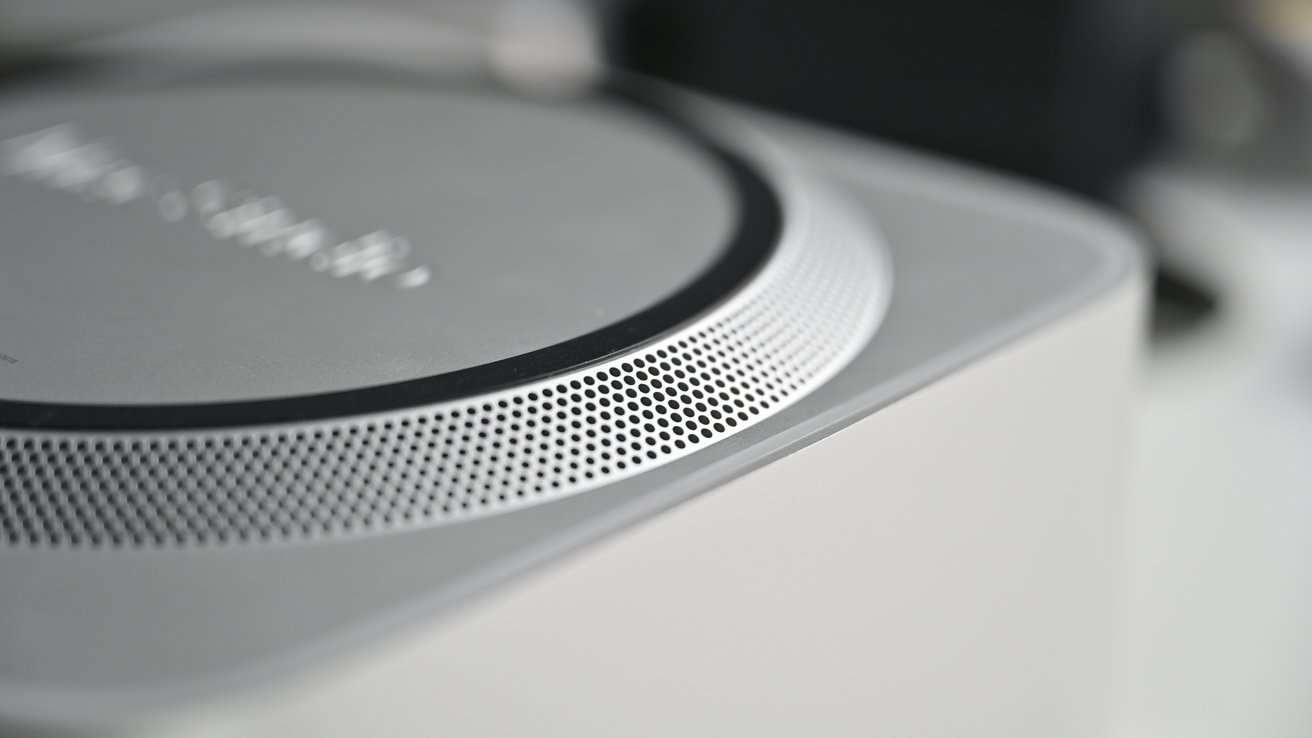 Close-up of a silver speaker with a perforated circular grille, showing detailed texture and blurred background.