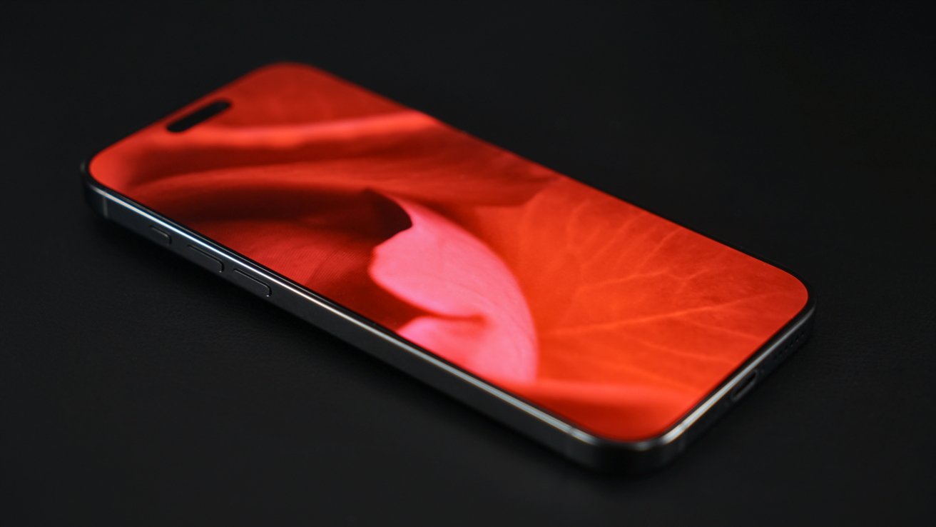 Smartphone with a vivid red petal close-up photograph on its screen, placed on a dark surface, viewed from an angle.